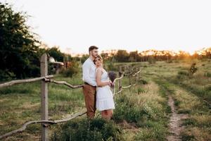 girl in a white sundress and a guy in a white shirt on a walk at sunset with a bouquet photo