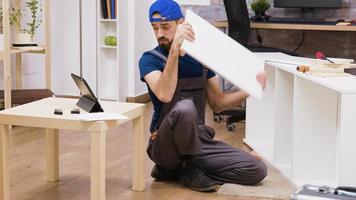 Male worker in overalls assembles new white furniture video