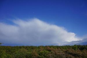 A huge fluffy cloud against the bright blue sky and moon photo