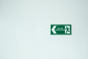 la señal de la ruta de evacuación en color verde está colgada en una pared blanca. el signo esencial de los lugares públicos. foto