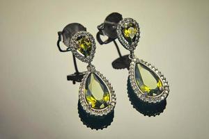 White gold earrings with diamonds and yellow-green stones on a gradient background with reflection. Jewelry production photo