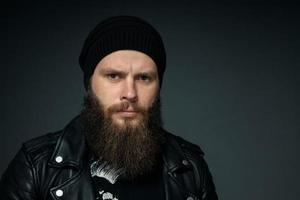 portrait of handsome bearded man in leather jacket and hat looking at the camera photo
