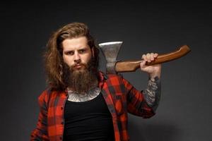 Hombre guapo con cabello largo con un hacha en sus manos sobre un fondo oscuro de estudio foto