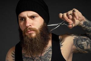 portrait of a courageous man with a beard he holds scissors near his beard and looks at the camera photo