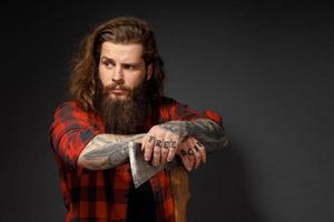 Hombre guapo con cabello largo con un hacha en sus manos sobre un fondo oscuro de estudio foto