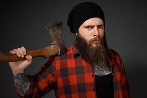 Hombre guapo con cabello largo con un hacha en sus manos sobre un fondo oscuro de estudio foto