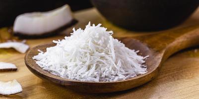 pieces of coconut, zest and chips on a rustic wooden table, culinary ingredient, with ripe coconut in the background