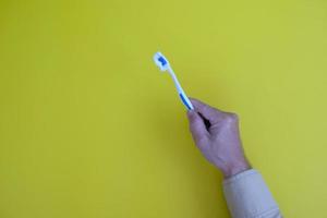 Hand holding a toothbrush with teeth isolated on a yellow backdrop with healthcare theme photo