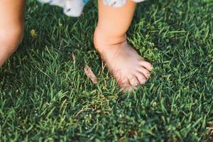 Feet baby child standing on green grass. Girl learn her senses with nature. Kid and sensory concept. photo
