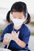 Kindergarten girl aged 4-5 years old wears white mask while taking simple food preservation class in nature classroom. New Normal. Prevent small dust pollution PM2.5 and virus epidemic. Vertical image photo