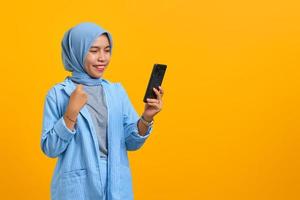 Cheerful young Asian woman looking at mobile phone isolated over yellow background photo