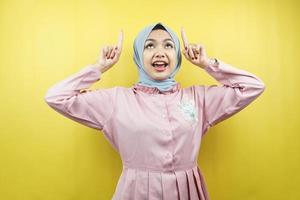 Cheerful beautiful young muslim woman, with hands pointing up, promoting something, isolated photo