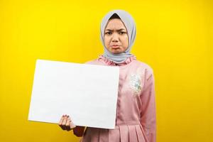 Bastante joven mujer musulmana triste, mano sosteniendo pancarta vacía en blanco, cartel, tablero blanco, tablero de letrero en blanco, tablero de anuncio blanco, presentando algo en el espacio de la copia, promoción foto