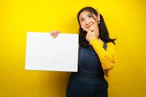 Pretty and cute young woman thinking, hand holding blank empty banner, placard, white board, blank sign board, white advertisement board, presenting something in copy space, promotion photo