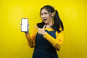 Pretty and cute young woman surprised, shocked, wow expression, hands holding smartphone, with blank or white screen smartphone, promoting app, promoting product, advertisement, isolated photo