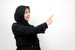 Beautiful asian young muslim woman with hands pointing empty space presenting something, smiling confident, enthusiastic, cheerful, facing empty space, isolated on white background
