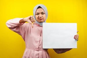 Bastante joven mujer musulmana no le gusta la mano, sosteniendo pancarta vacía en blanco, cartel, tablero blanco, tablero de letrero en blanco, tablero de anuncio blanco, presentando algo en el espacio de la copia, promoción foto