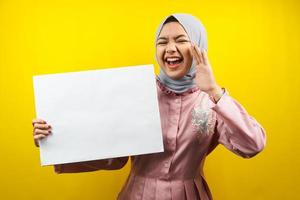Bastante joven mujer musulmana alegre sosteniendo pancarta vacía en blanco, cartel, tablero blanco, tablero de letrero en blanco, tablero de anuncio blanco, presentando algo en el espacio de la copia, promoción foto