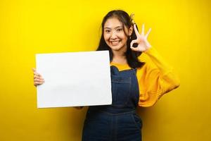 Bonita y linda mujer joven alegre sosteniendo pancarta vacía en blanco, cartel, tablero blanco, tablero de letrero en blanco, tablero de anuncio blanco, presentando algo en el espacio de la copia, promoción foto