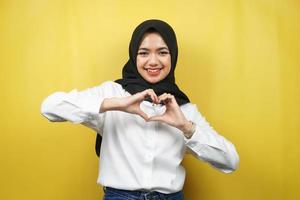 Hermosa joven musulmana asiática sonriendo confiada, entusiasta y alegre con las manos en señal de amor, afecto, feliz, en el pecho aislado sobre fondo amarillo foto