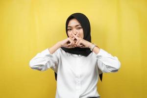 Beautiful asian young muslim woman with finger on mouth, telling to be quiet, don't make noise, lower your voice, don't talk, isolated on yellow background photo