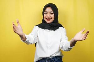 Beautiful young asian muslim woman smiling cheerfully, with open arms to camera, welcome sign hand, hand sign wanting to hug, isolated on yellow background photo