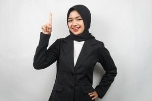 Beautiful young asian muslim business woman confident and smiling, with hands pointing up, getting ideas, presenting something, isolated on gray background photo