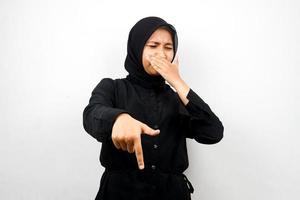 Beautiful young muslim woman with hand covering mouth, hand pointing down, showing disapproval expression, showing disgust at something, isolated on white background photo