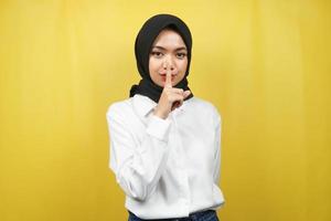 Hermosa joven musulmana asiática con el dedo en la boca, diciendo que se calle, no hagas ruido, baja la voz, no hables, aislado sobre fondo amarillo