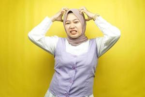 Beautiful young asian muslim woman shocked, dizzy, stressed, unhappy, many problems, want solution, with  hands holding head isolated on yellow background photo