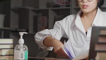 Serious Asian young woman wearing glasses, sitting and looking at revenue paper, getting tired and throwing it up. Getting headache, touching head. Losing money from doing selling online video