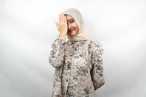 Hermosa joven musulmana asiática con la mano cubriendo un ojo mirando a la cámara aislada sobre fondo blanco.