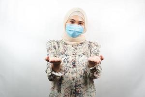 Mujer musulmana vistiendo máscara médica, manos presentando algo, aislado sobre fondo blanco. foto