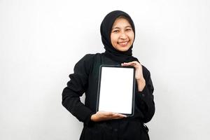 Hermosa joven mujer musulmana asiática sonriendo, tableta de mano con pantalla blanca o en blanco, promoción de aplicaciones, promoción de productos, presentando algo, emocionado y alegre, aislado sobre fondo blanco. foto