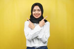 Beautiful young asian muslim woman smiling confident, enthusiastic, cheerful with hands pointing  empty space presenting something, looking at camera isolated on yellow background, advertising concept photo