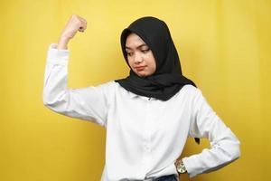 Hermosa joven musulmana asiática con músculos levantados, brazos de signo de fuerza, aislado sobre fondo amarillo foto