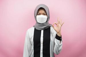 mujer musulmana con máscaras blancas, movimiento contra el virus corona, movimiento anti covid-19, movimiento de salud con máscaras, con las manos mostrando el signo de ok, buen trabajo, éxito, victoria, aislado sobre fondo rosa foto