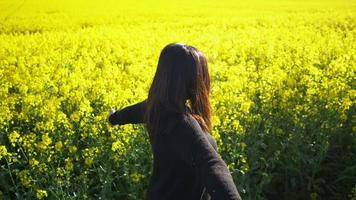 mujer asiática de pie, dándose la vuelta y levantando las manos en el campo amarillo, sonriendo y tomando un poco de aire fresco con buena naturaleza. buen tiempo y cielo azul claro. fondo de campo amarillo