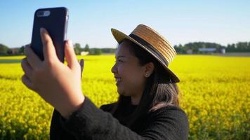 Close up happy Asian woman taking video call in yellow field, showing beautiful view, enjoying Nice Nature. Asian woman smiling. Good weather and clear blue Sky. Holiday concept