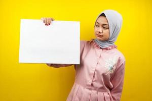 Pretty young muslim woman holding blank empty banner, placard, white board, blank sign board, white advertisement board, presenting something in copy space, promotion photo