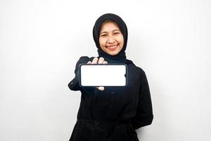 Beautiful young asian muslim woman smiling confident, enthusiastic and cheerful with hands holding smartphone, promoting application, promoting game, isolated on white background, advertising concept