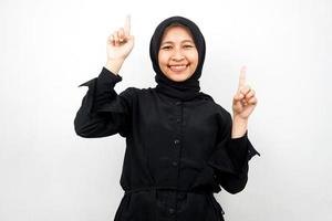 Beautiful young asian muslim woman smiling confident, enthusiastic and cheerful with hands pointing up presenting something, looking at camera isolated on white background, advertising concept photo