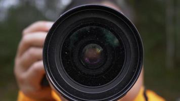 fotógrafo sosteniendo una cámara y tomando una foto en el bosque. tomar una foto al aire libre. vista frontal de enfoque y disparo. cerrar cámara lenta video