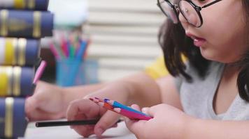 primo piano ragazza asiatica che dipinge con il colore della matita su carta con la mamma. sedersi e fare arte sul tavolo di casa. stare a casa durante il fine settimana concept video