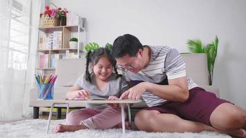 Happy Asian father playing with daughter having fun spending free leisure time painting on paper. Having a funny conversation. Painting with color pencil in living room at home. Happy fat family video