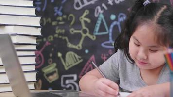 Nahaufnahme asiatisches Mädchen, das Laptop und Bücher betrachtet und mit Bleistiftfarbe auf Papier malt. Mädchen, das zu Hause sitzt und Kunst auf dem Tisch macht. am Wochenende zu Hause bleiben Konzept video