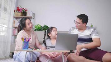 Happy Asian family sitting on the floor in living room and spending time having funny conversation. Putting laptop on the table. Daughter, mom and dad. Happy family concept video
