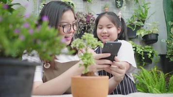 Asian cute child girl and mom taking a picture of plants that they growing in the garden at home. Happy family on weekend. Gardening concept video