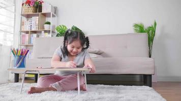 gelukkig dik Aziatisch meisje zittend op de vloer en schilderen op papier op de tafel in de woonkamer, met behulp van kleurpotlood. huiswerk maken, kunstvak. thuisblijven in het weekend concept video