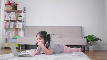 gelukkig Aziatisch meisje dat op de vloer ligt, videogesprek aanneemt op laptop en draadloze microfoon gebruikt in de woonkamer, typt op toetsenbord tijdens videogesprek. thuisblijven concept